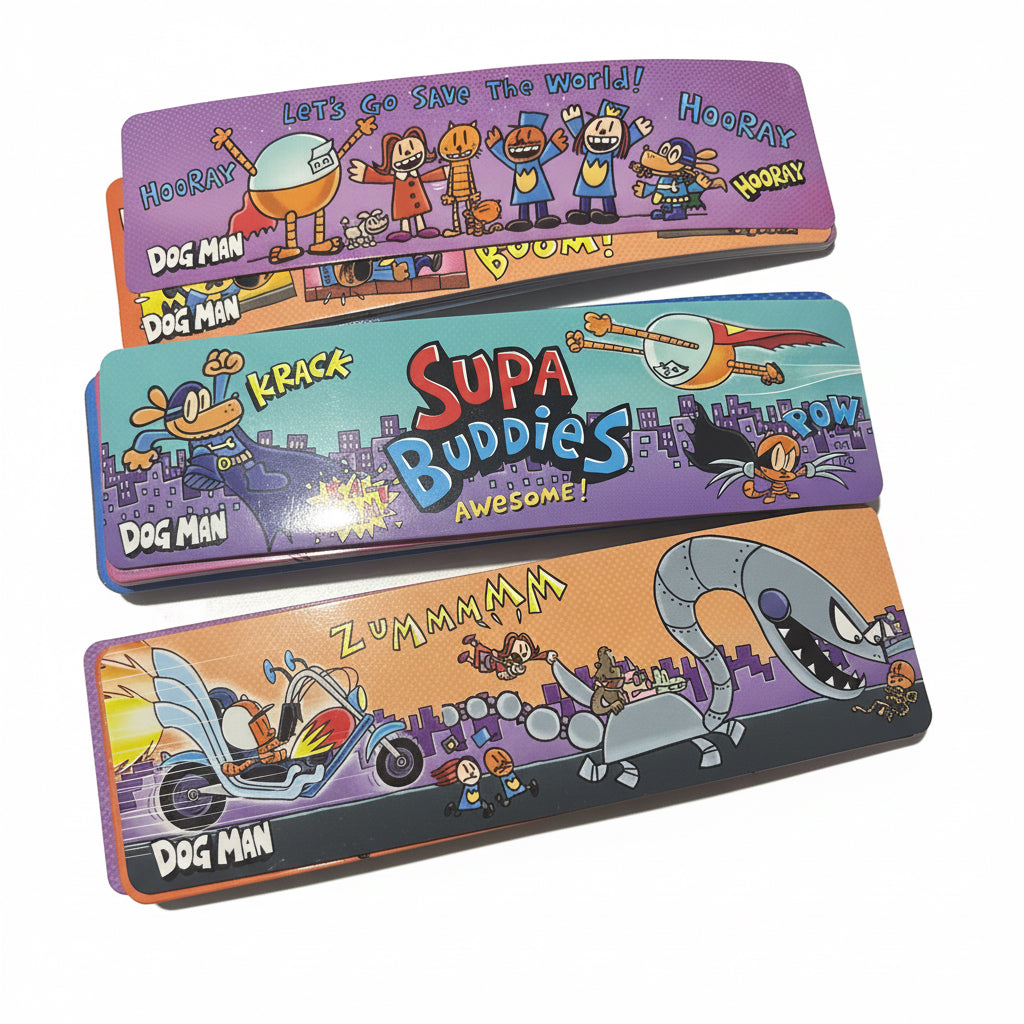Three colorful metal dog toy paddles with cartoon graphics and text, stacked vertically on a light surface. The paddles feature characters and words like 'Dog Man', 'Krack', 'Supa Buddies', and 'Zummma'.